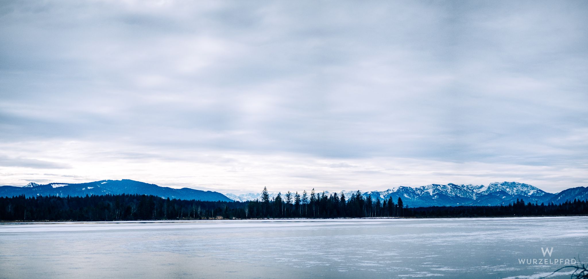 Blick über den eingefrorenen Kirchsee in den Isarwinkel